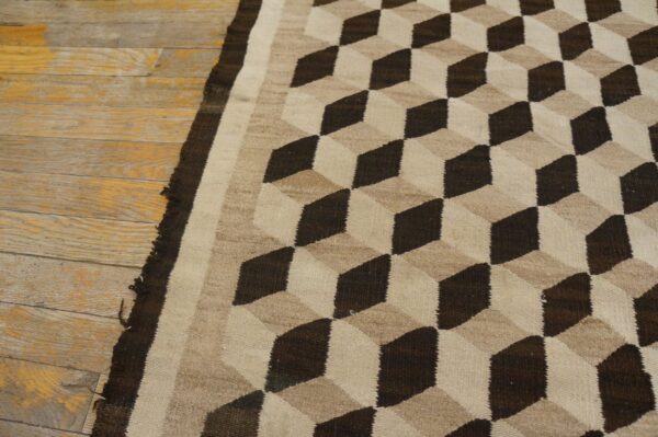 Dark brown and beige flatweave rug with an optical cube pattern on rustic wooden flooring.