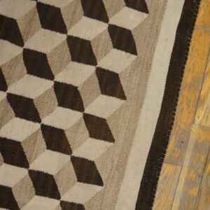 Dark brown and beige tumbling block patterned flatweave rug lies partially on worn wooden floorboards.