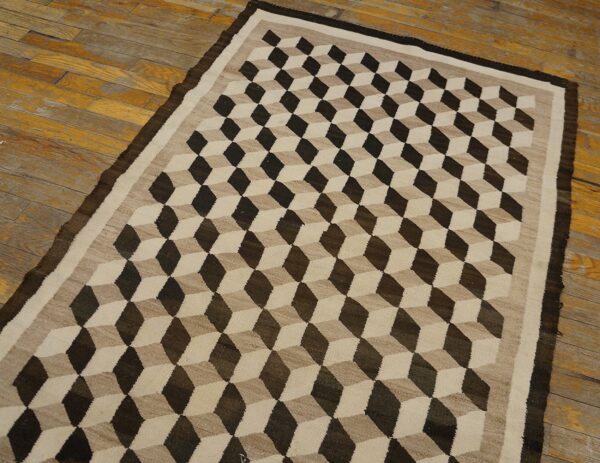 Flatwoven rug in dark brown, tan, and beige with a geometric cube pattern on distressed wood floor.