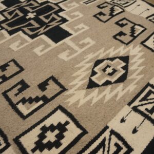 Flatwoven rug featuring bold black, cream, and tan geometric patterns resting on wood flooring.