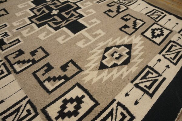 Flatwoven rug featuring bold black, cream, and tan geometric patterns resting on wood flooring.