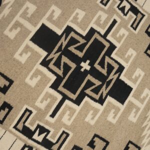 Flatweave rug texture visible with black, light tan, and cream interlocking geometric shapes.