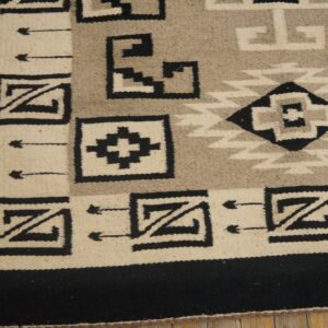 A black, cream, and gray geometric flatweave rug rests on distressed wooden floorboards.