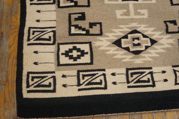 A black, cream, and gray geometric flatweave rug rests on distressed wooden floorboards.