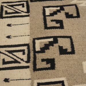 Flatweave rug featuring black, cream, and taupe stepped geometric patterns on a wood floor.