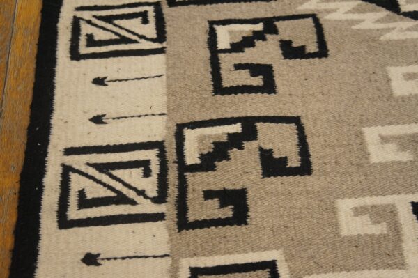 Flatweave rug featuring black, cream, and taupe stepped geometric patterns on a wood floor.