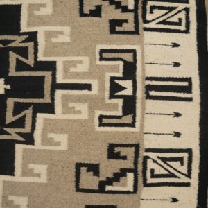 Geometric flatweave rug in black, gray, and cream, featuring crosses and angular borders on distressed wooden floor.