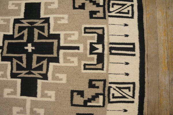 Geometric flatweave rug in black, gray, and cream, featuring crosses and angular borders on distressed wooden floor.