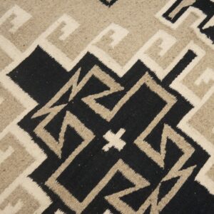 Flat woven rug featuring a black, cream, and tan interlocking stepped geometric pattern.