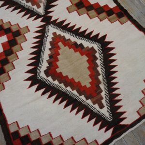 Cream flatweave rug with a large central serrated diamond motif in brown, red, and tan colors.