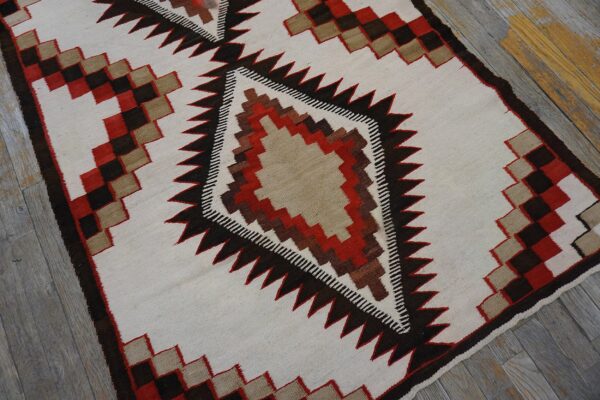 Cream flatweave rug with a large central serrated diamond motif in brown, red, and tan colors.