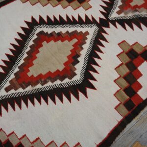 Geometric flatweave rug featuring cream, dark brown, tan, and red serrated diamonds on gray wood flooring.