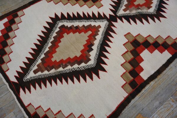 Geometric flatweave rug featuring cream, dark brown, tan, and red serrated diamonds on gray wood flooring.