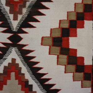 Geometric flatweave rug section featuring red, tan, black, and cream patterns next to distressed wood.