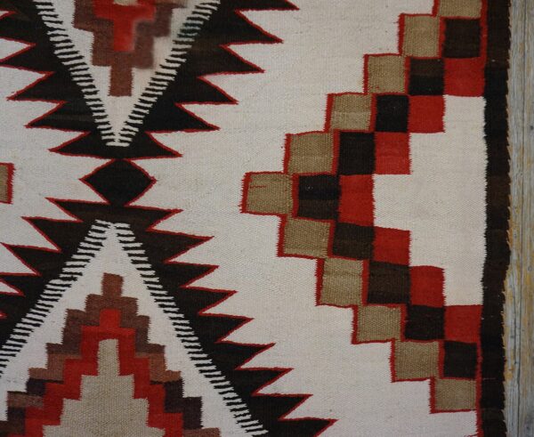 Geometric flatweave rug section featuring red, tan, black, and cream patterns next to distressed wood.