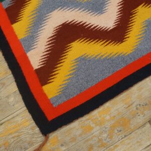 Geometric flatwoven rug in yellow, blue, brown, and red on distressed wood flooring.
