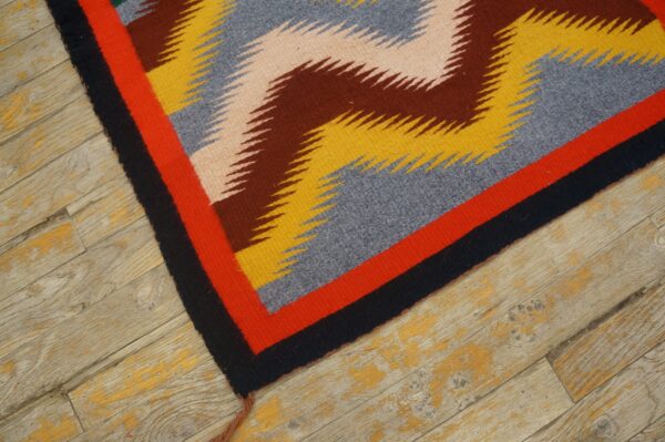 Geometric flatwoven rug in yellow, blue, brown, and red on distressed wood flooring.