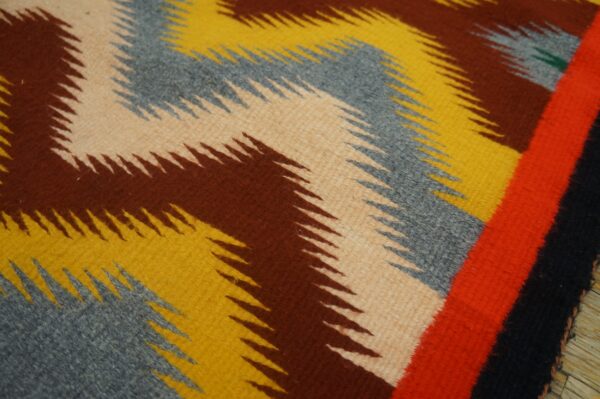 Woven rug featuring thick zigzag stripes in tan, brown, yellow, and gray, with a bright red border detail.