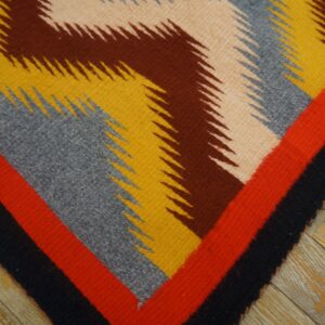 Jagged geometric flatweave rug in red, black, yellow, gray, and brown colors lying on distressed wood planks.