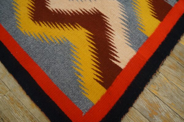 Jagged geometric flatweave rug in red, black, yellow, gray, and brown colors lying on distressed wood planks.