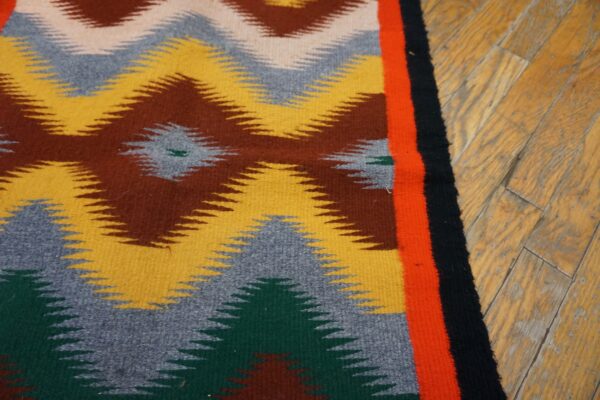 Low-pile rug with geometric zig-zags in yellow, brown, and gray, bordered by orange and black on wood.