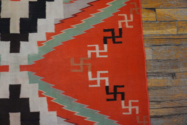 Red, black, and white flatweave rug with geometric symbols and zigzag patterns on distressed wood.
