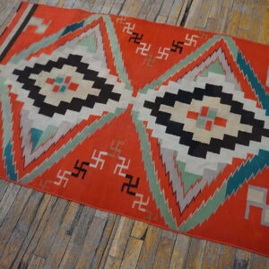 Orange flatweave rug displays large black, white, and mint geometric diamonds on rustic wooden floorboards.