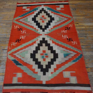 Orange flatweave rug displaying large concentric diamond designs and geometric symbols on a distressed wood floor.