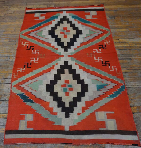 Orange flatweave rug displaying large concentric diamond designs and geometric symbols on a distressed wood floor.