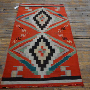 Orange flatweave rug with stepped diamonds and repeating geometric symbols on rustic wood planks.