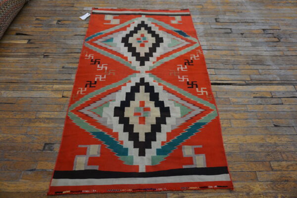 Orange flatweave rug with stepped diamonds and repeating geometric symbols on rustic wood planks.