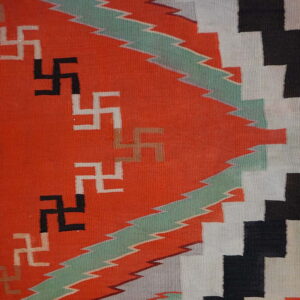 Geometric flatweave rug in orange, black, white, and mint green with repeating hooked cross symbols on wood floors.