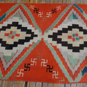 Orange flatweave rug displaying large black and white geometric diamonds and scattered stepped symbols on wood.