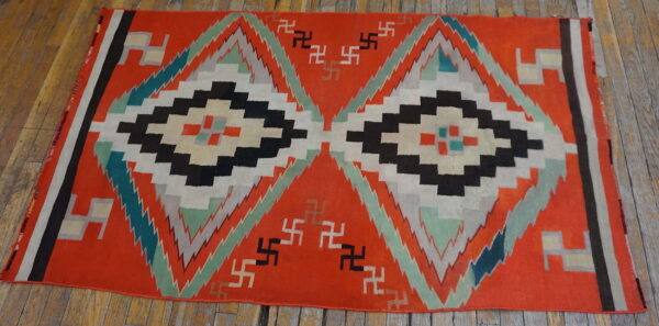 Orange flatweave rug displaying large black and white geometric diamonds and scattered stepped symbols on wood.