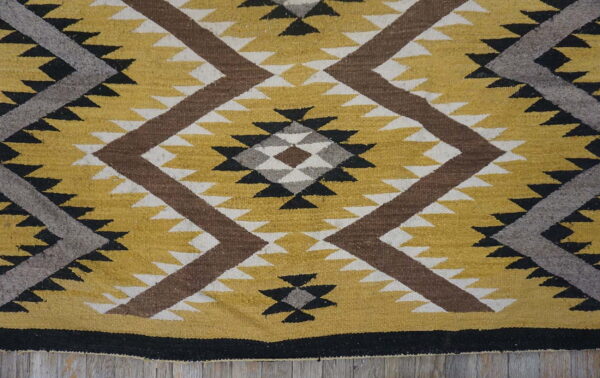 Mustard yellow, brown, gray, and black diamond-patterned flat-woven rug on wood flooring.