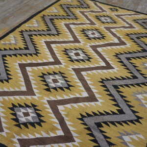 Mustard yellow rug featuring large brown, gray, black, and white zigzag patterns on distressed wood flooring.