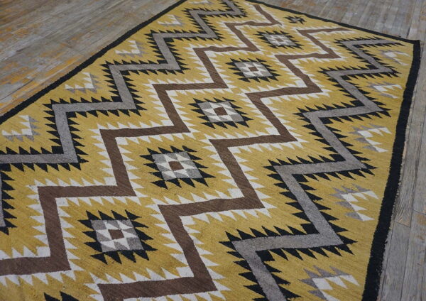 Mustard yellow rug featuring large brown, gray, black, and white zigzag patterns on distressed wood flooring.