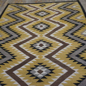 A yellow, brown, and grey flatweave rug with zig-zag and diamond patterns rests on rustic wood flooring.