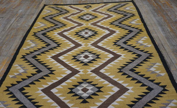 A yellow, brown, and grey flatweave rug with zig-zag and diamond patterns rests on rustic wood flooring.