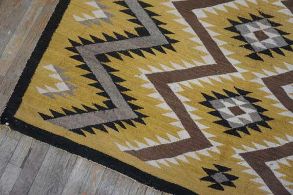 Geometric yellow, brown, gray, and black rug with serrated zigzag patterns lying on gray wood floor.