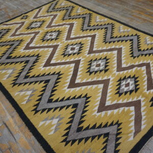 Geometric low-pile rug in yellow, brown, gray, and black zigzag patterns over distressed wood floorboards.