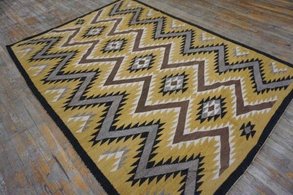 Geometric low-pile rug in yellow, brown, gray, and black zigzag patterns over distressed wood floorboards.