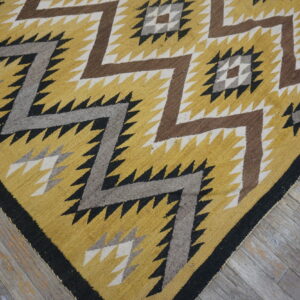 Low-pile rug in yellow, brown, gray, and black with sharp geometric zig-zags on weathered wood.