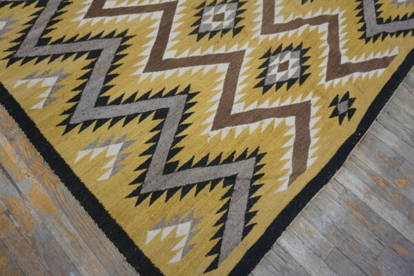 Low-pile rug in yellow, brown, gray, and black with sharp geometric zig-zags on weathered wood.