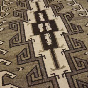 Geometric rug in sage, cream, and dark brown featuring zigzags and spirals on wooden floorboards.