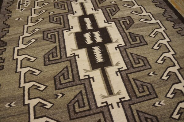 Geometric rug in sage, cream, and dark brown featuring zigzags and spirals on wooden floorboards.