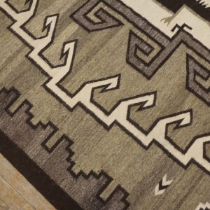 Flat-woven rug with dark brown, cream, and moss green geometric motifs on rustic wood floor.