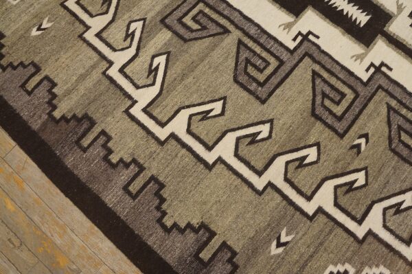 Flat-woven rug with dark brown, cream, and moss green geometric motifs on rustic wood floor.