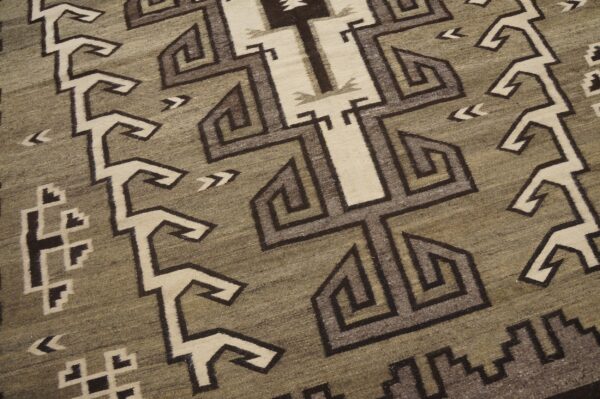 Low-pile rug detail showing geometric interlocking patterns in khaki, cream, and shades of brown.