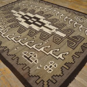 Geometric rug in neutral taupe, dark brown, and cream with a low pile on distressed wood flooring.